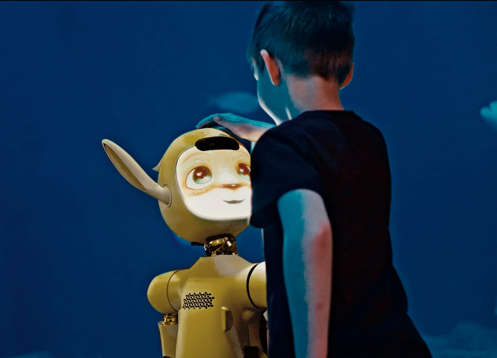 A boy gently patting the head of a friendly yellow robot, which looks up at him and smiles