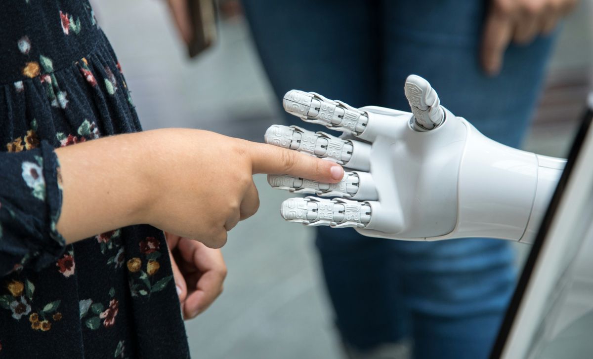 A child reaching out to touch the fingers of a white robot hand