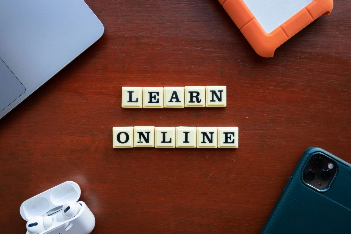 Letter tiles spelling LEARN ONLINE on a desk beside a laptop, phone and earbuds