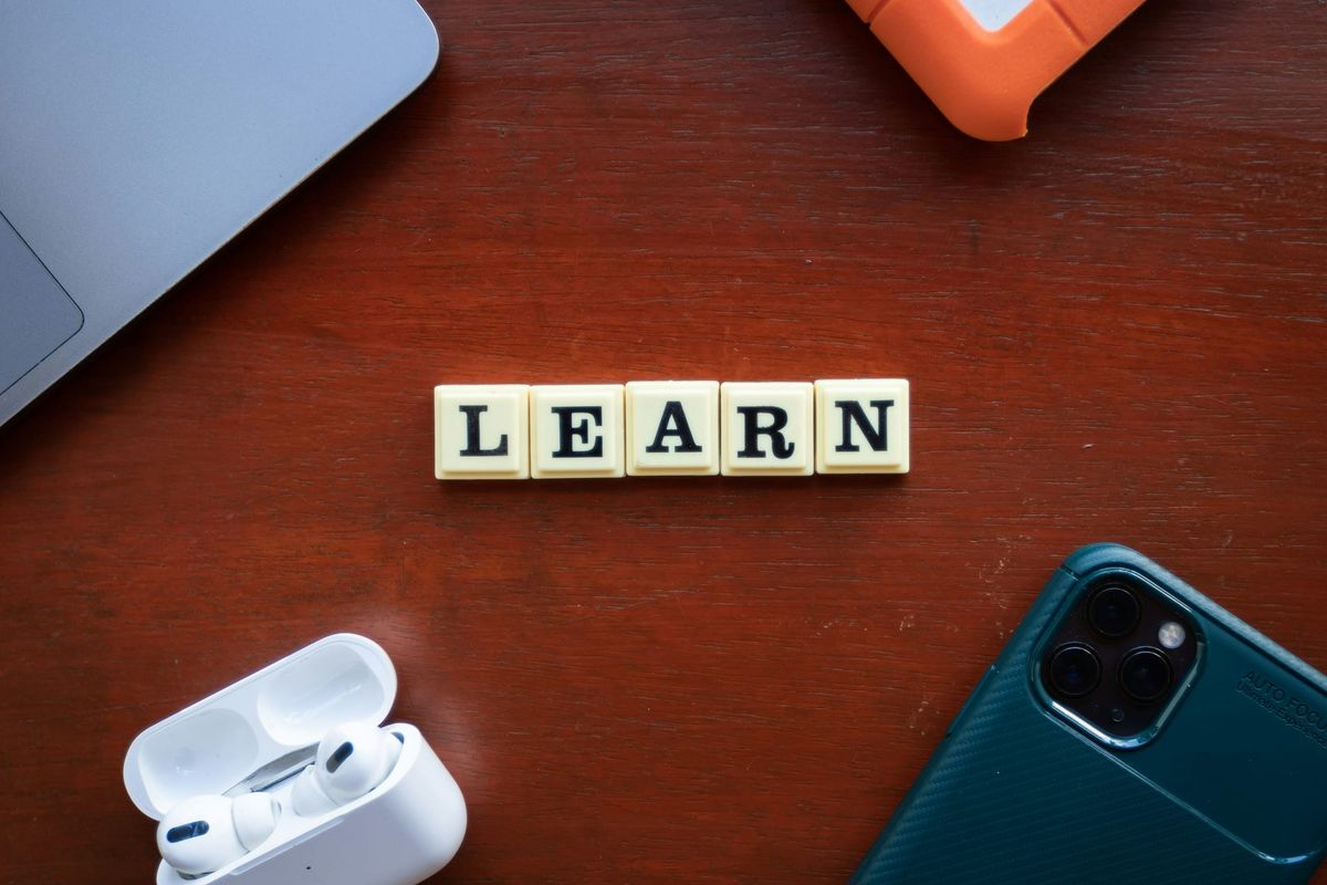 Letter tiles spelling LEARN on a wooden desk beside a laptop and a phone