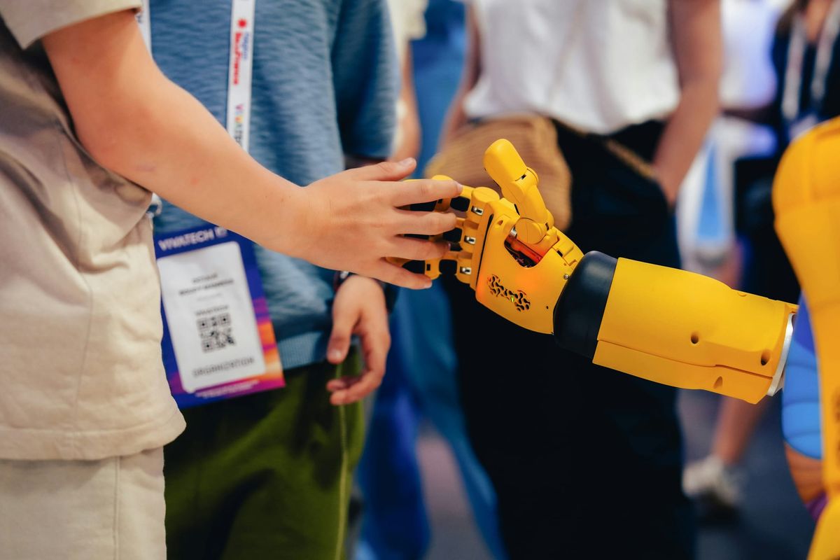 A child's hand meeting a robot's hand, fingers interlocked